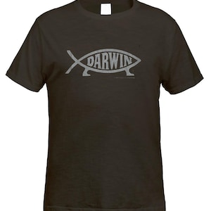 Puede incluir: Una camiseta de manga corta de color marrón oscuro con un gráfico gris claro de un pez con patas. La palabra DARWIN está impresa en letras mayúsculas dentro del cuerpo del gráfico del pez, situado en el centro del pecho de la prenda.