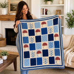 Peut inclure: Une couverture rectangulaire en crochet avec un motif en damier composé de carrés bleu clair, bleu moyen et bleu foncé. Le design inclut des champignons rouges appliqués à pois blancs et des motifs d'arbres bleu clair, bordée de pompons blancs.