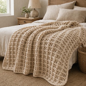 Peut inclure: Une couverture beige à mailles épaisses drapée sur un lit. La couverture présente un motif tissé texturé et est faite d'un matériau doux et épais. Le lit a une tête de lit en bois et est recouvert d'une literie de couleur neutre. Un panier en osier est au pied du lit.