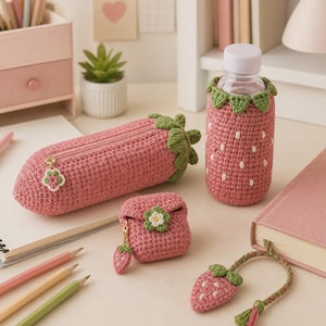 Peut inclure: Un ensemble d'accessoires en crochet sur le thème de la fraise comprenant une trousse rose avec fermeture éclair, une housse de bouteille, un petit étui carré pour écouteurs avec une breloque fleur et un marque-page en forme de fraise.