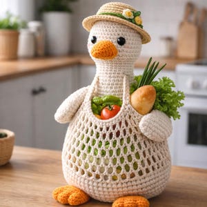 May include: A crocheted goose figure wearing a straw hat with yellow flowers. The goose has an orange beak and feet, and carries a mesh bag filled with vegetables, including a tomato, lettuce, and a carrot. The goose is on a wooden surface.