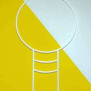 Puede incluir: Un adorno para pastel de metal blanco con un círculo grande en la parte superior, conectado a una base rectangular de tres niveles con dos estacas puntiagudas. El fondo está dividido diagonalmente, con secciones amarillas y blancas.