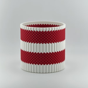 May include: A cylindrical container featuring alternating horizontal bands of white and red. The white sections have a vertical ribbed texture, while the red sections display a raised, diamond-shaped grid pattern throughout the exterior.