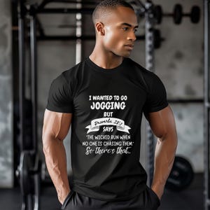 May include: Black t-shirt with white text: "I WANTED TO GO JOGGING BUT Proverbs 28:1 SAYS 'THE WICKED RUN WHEN NO ONE IS CHASING THEM' So there's that..." The shirt is worn by a person in a gym setting.