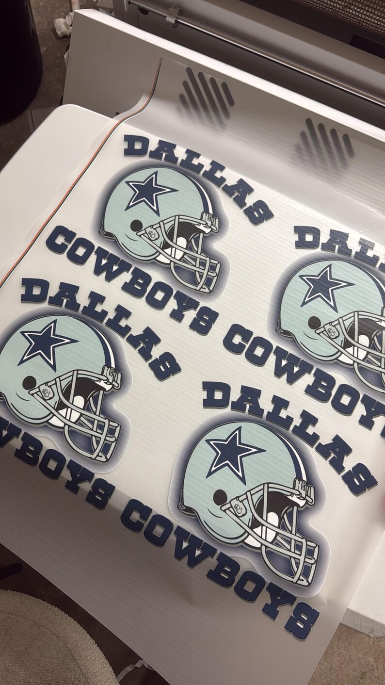 K&ouml;nnte beinhalten: Bogen mit Aufklebern von Dallas Cowboys-Helmen. Die Aufkleber zeigen einen hellblauen Helm mit einem marineblauen Stern und den Worten "DALLAS COWBOYS" in Marineblau. Auf wei&szlig;em Hintergrund.