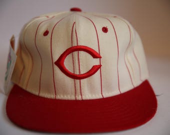 May include: Cream-colored baseball cap with red pinstripes and a red brim. The cap features a red embroidered "C" logo on the front. A small tag is attached to the side. This vintage-style hat is a classic sports accessory.