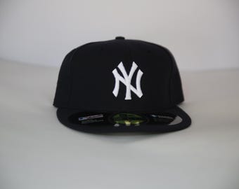 Puede incluir: Gorra de béisbol negra con visera plana. La gorra presenta el logotipo blanco entrelazado "NY" en la parte delantera. Esta gorra clásica es adecuada para deportes o uso informal. Un accesorio popular.