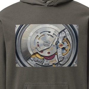 May include: A gray hoodie with a close-up image of a watch mechanism on the front. The watch mechanism is silver with gold and red accents. The hoodie has a hood and a front pocket.