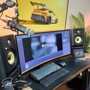 Può includere: Un moderno allestimento per l'home office con un monitor curvo che mostra il logo "Bambu Lab", una tastiera meccanica e un mouse. Due altoparlanti da studio neri con coni gialli affiancano il monitor. Sono visibili anche un microfono e un'immagine di un'auto sportiva gialla.