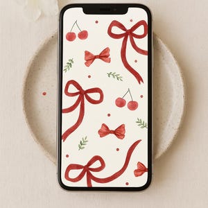 Könnte beinhalten: Ein Smartphone zeigt ein skurriles Muster aus roten Bändern, Kirschen und grünen Zweigen auf cremefarbenem Hintergrund. Das Telefon liegt auf einem beigen Teller, mit einer weißen Blume in der Nähe.