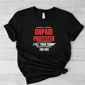以下が含まれることがあります： 赤い文字で「UNPAID PROTESTER」と「I YELL 'FUCK TRUMP' FOR FREE」と書かれた黒いTシャツ。Tシャツは柔らかい素材でできており、半袖です。