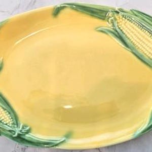 May include: Oval-shaped yellow ceramic serving platter with green corn and leaf detailing around the edges. The platter has a glossy finish and is designed with three corn cobs and leaves. A decorative piece for serving food.