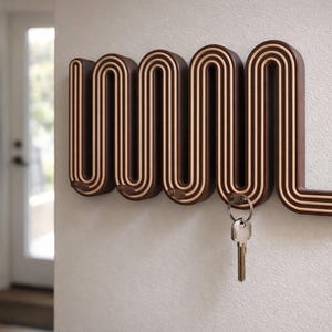 May include: A brown and beige wall-mounted key holder with a unique, wavy design. The key holder has a series of curved sections with a lighter-colored interior, and a set of keys is hanging from one of the hooks. The key holder is mounted on a white wall.