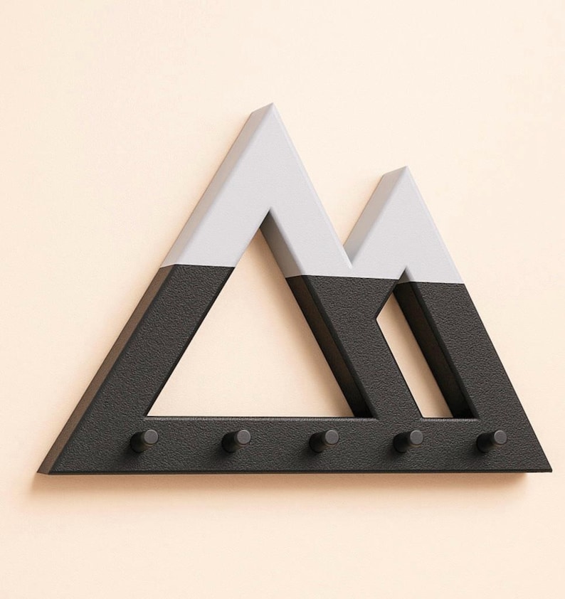 Mountain key holder in black and gray seen from the front, textured base and light gray peaks on a pale peach wall