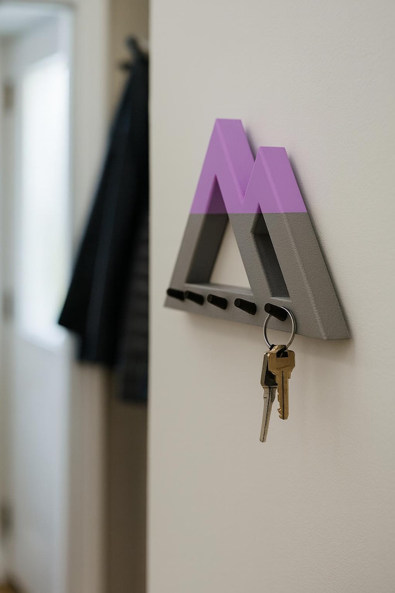 Mountain key holder in gray and purple, side view with brass keys on the end peg and a dark coat hanging by the door