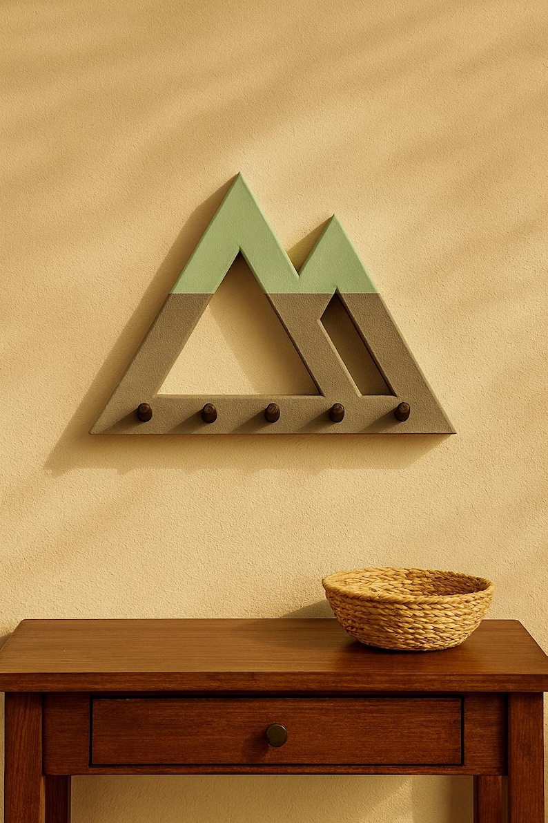 Mountain key holder in gray and sage green on a warm beige wall above a wooden console table with a woven basket