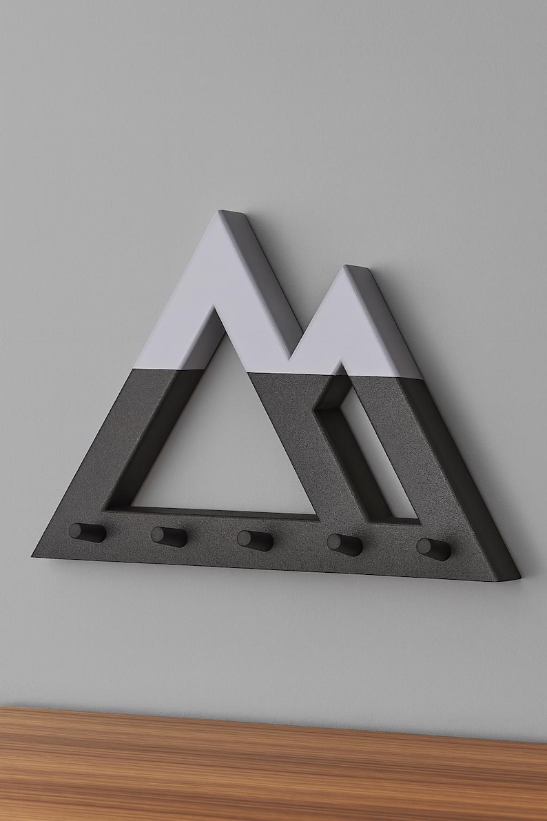 Black Mountain key holder with light gray peaks, angled on a gray wall above a wood surface, all five pegs empty