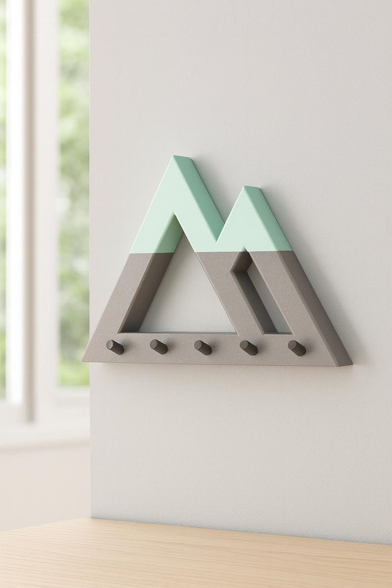 Gray and mint green Mountain key holder on a pale wall beside a sunny window, five empty pegs at a slight angle