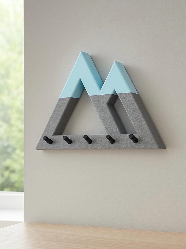 Gray and teal Mountain key holder on a light gray wall, angled to show its depth and five empty black pegs, a window at left