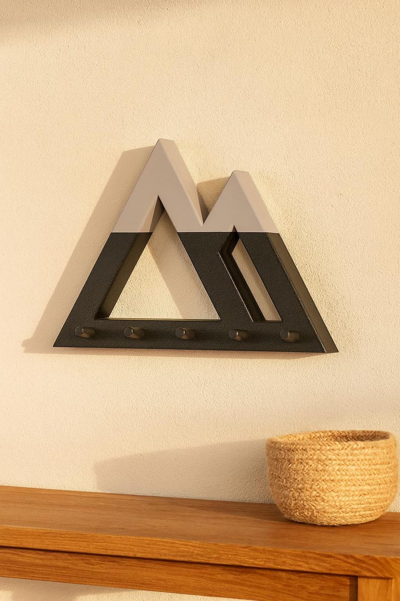 Black and gray Mountain key holder in warm sunlight above a wooden console table with a woven basket