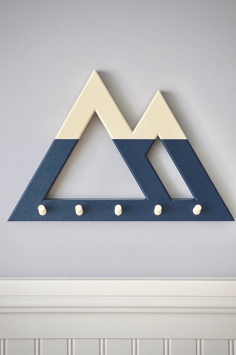 Blue and white Mountain key holder straight on above white beadboard wainscoting, a plain lilac-gray wall around it