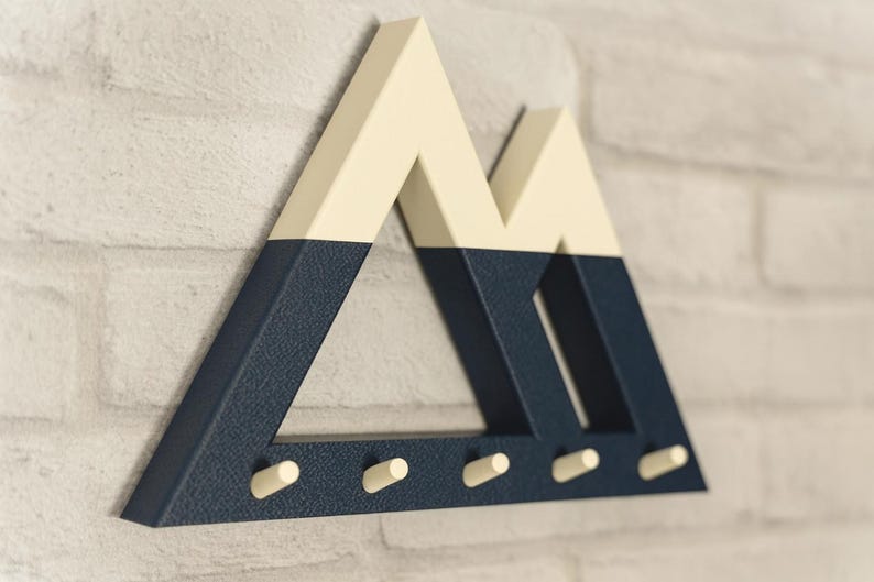Blue and white Mountain key holder angled on a whitewashed brick wall, its five cream pegs empty