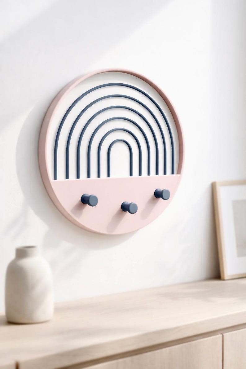 Pink Boho key holder with dark blue arches above a light wood sideboard, a white ceramic vase and a framed print on top