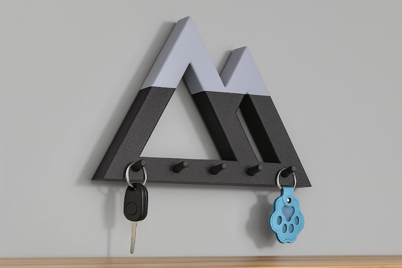 Mountain key holder in black and gray on a gray wall, a car key and a blue paw-shaped key fob on the end pegs