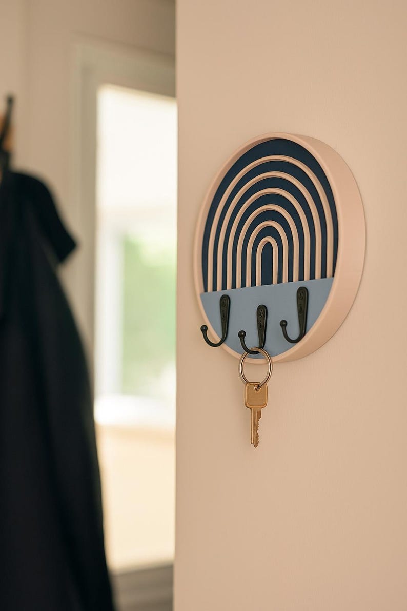 Dark blue Boho key holder on a warm blush wall with a brass key, a dark coat hanging by a bright doorway behind