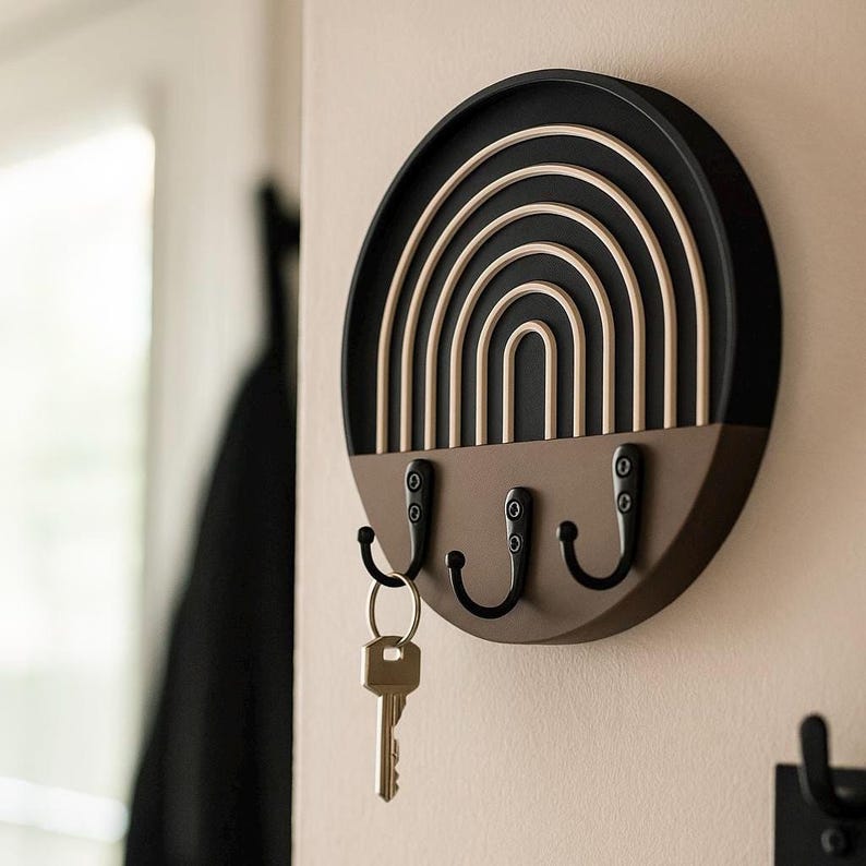 Black Boho key holder in side view showing its depth, a single brass key on the left hook and a black coat behind