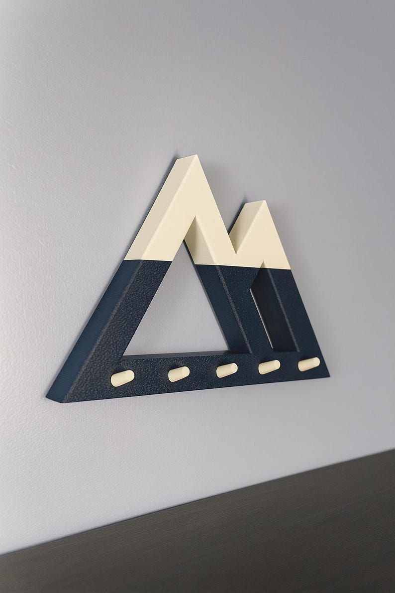 Blue and white Mountain key holder from a low side angle on a pale lilac-gray wall above a dark shelf, showing its depth