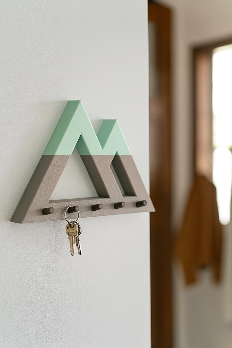 Mountain key holder in gray and mint green on a white wall by a wooden doorway, house keys on the second of five pegs