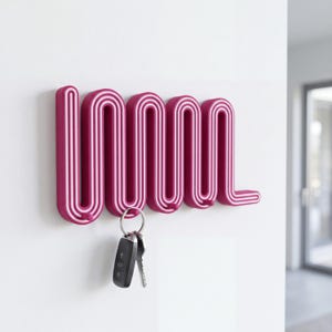 Puede incluir: Un perchero de pared con rayas magenta y blancas en forma de serpiente continua. El perchero cuenta con varios ganchos redondeados a lo largo del borde inferior, con un juego de llaves de metal colgado de uno de los ganchos del lado izquierdo.