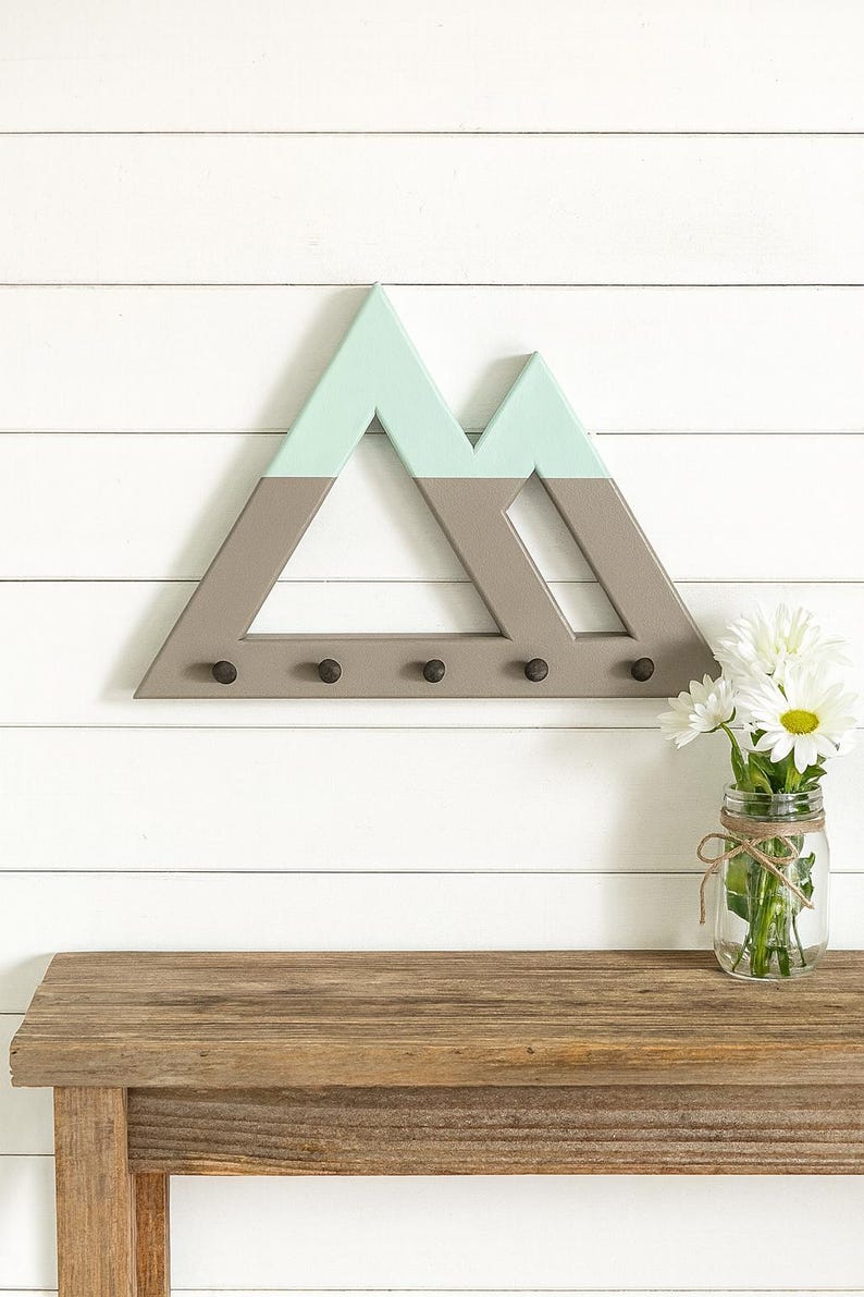 Mountain key holder in gray and green on white shiplap above a rustic wood table, a mason jar of daisies beside it