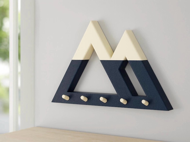 Blue and white Mountain key holder at an angle, showing its textured navy finish, cream-white peaks and five pegs