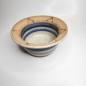 Puede incluir: Cuenco de cerámica hecho a mano con interior blanco moteado y diseño de rayas azules. El borde es de color marrón claro con recortes triangulares. Una pieza única para servir o exhibir.