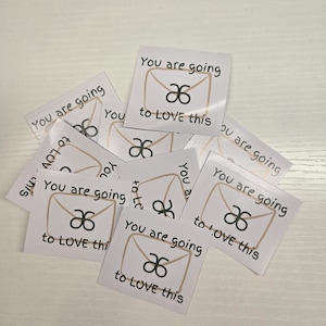 May include: Several white square stickers with the text "You are going to LOVE this". Each sticker has a beige envelope design and a black symbol. The stickers are arranged on a white surface.