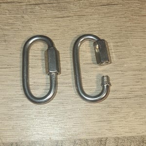 May include: Two silver-colored, heavy-duty carabiner clips. One is closed, and the other is open, showing the threaded screw gate. The clips are made of metal and are designed for secure fastening.