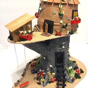 May include: A miniature treehouse structure featuring a dark gray textured trunk base, a tan dome-shaped upper dwelling with a shingled roof, a small wooden shed, a red swing, a black ladder, and decorative floral accents with tiny butterflies.