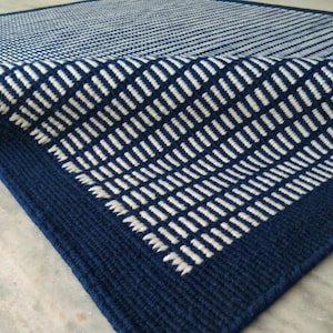 Puede incluir: Una alfombra rectangular con una base de color azul marino profundo y un patrón repetitivo de guiones blancos horizontales cortos dispuestos en columnas verticales. La alfombra tiene un borde azul marino sólido y textura tejida.