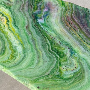 May include: Abstract art piece with a vibrant, flowing design. The artwork features a blend of green hues, with streaks of yellow, purple, and white, creating a marbled effect. The colors swirl together, giving the piece a dynamic and organic feel.