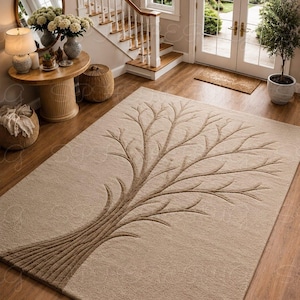 May include: A rectangular area rug in a light beige tone featuring a raised, textured brown tree design that extends from the bottom left corner across the surface. The rug has a soft, plush pile and is positioned on a wooden floor in a hallway.