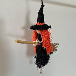 Puede incluir: Muñeca de bruja de Halloween hecha a mano, con sombrero puntiagudo negro, pelo naranja y vestido negro. La bruja sostiene una escoba de madera y está hecha de hilo. Decoración festiva para Halloween.