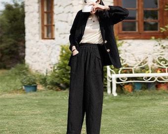 Puede incluir: Una persona con una blazer negra con botones dorados, una camiseta color crema y pantalones negros de pernera ancha. La persona también lleva una gorra de béisbol blanca y zapatillas blancas. El atuendo se usa al aire libre en un césped.