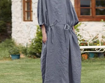 May include: A long, gray linen dress with a round neckline and short, wide sleeves. The dress features a drawstring waist and pockets. The model is wearing brown leather shoes. The dress is suitable for casual wear.