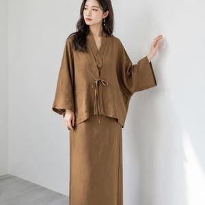 May include: A brown two-piece set consisting of a long-sleeved, open-front jacket with a tie closure at the waist and a matching ankle-length skirt. The jacket features wide sleeves and a V-neckline, while the skirt has a straight, simple cut.