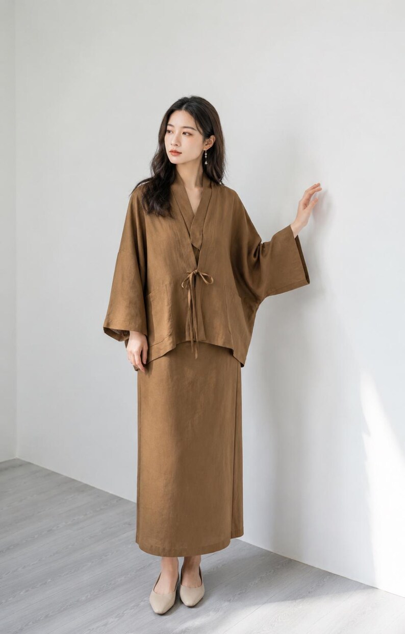 May include: A brown two-piece set consisting of a long-sleeved, open-front jacket with a tie closure at the waist and a matching ankle-length skirt. The jacket features wide sleeves and a V-neckline, while the skirt has a straight, simple cut.