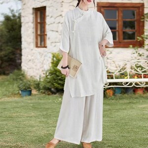 May include: A cream-colored linen outfit consisting of a tunic top and wide-leg pants. The top has a mandarin collar and three-quarter sleeves. The outfit is paired with brown flats. The ensemble is suitable for casual wear.