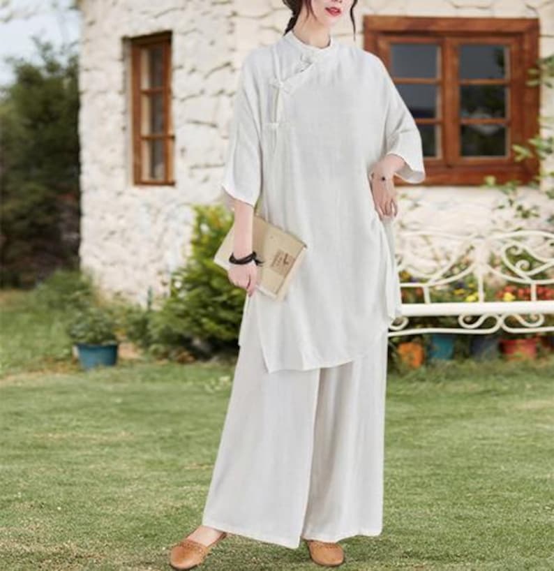 May include: A cream-colored linen outfit consisting of a tunic top and wide-leg pants. The top has a mandarin collar and three-quarter sleeves. The outfit is paired with brown flats. The ensemble is suitable for casual wear.