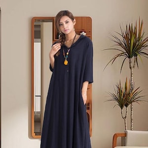 May include: A navy blue maxi dress with a hood and short sleeves. The dress has a relaxed fit and pockets. A colourful necklace adds a pop of colour. The dress is suitable for casual wear.
